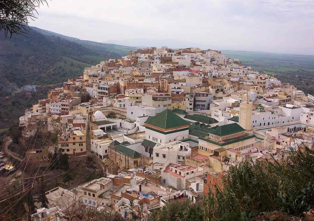 View of the sacred town of Moulay Idriss with its white buildings and green hills in Morocco.